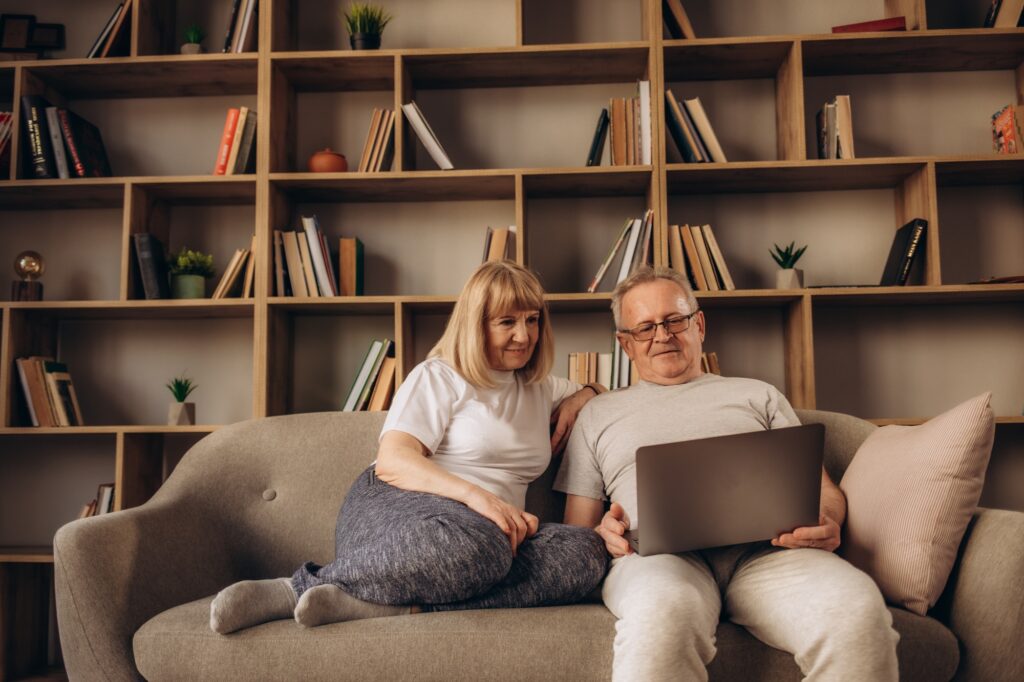 Mature man and woman using laptop together, looking at screen, older spouses browsing apps, shopping