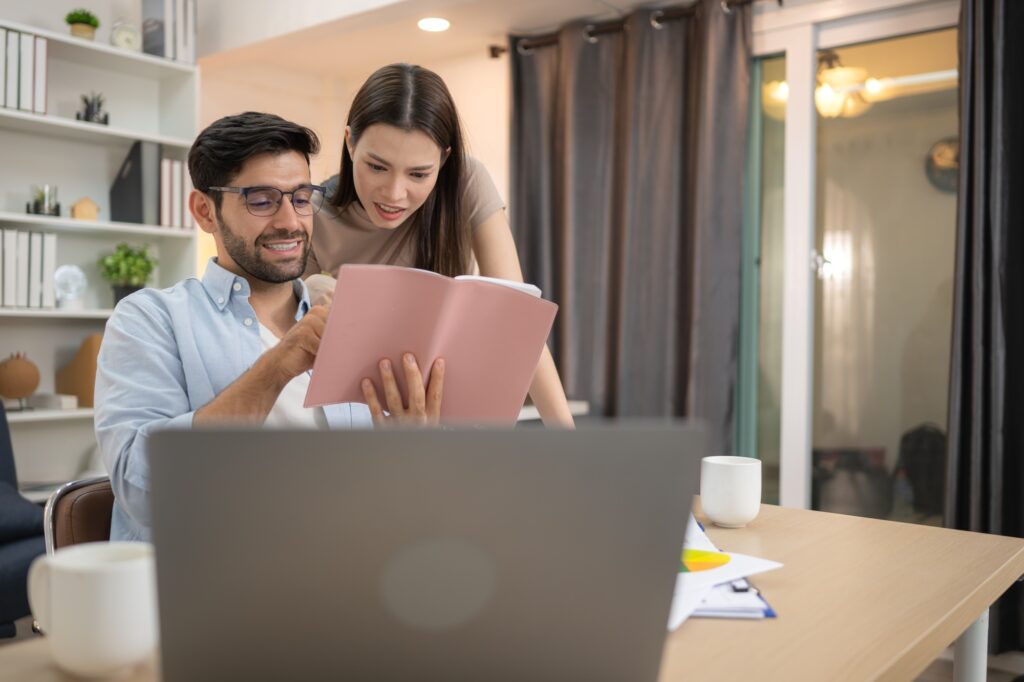 Portrait of a young freelancer smiling while working online via laptop at home with his girlfriend